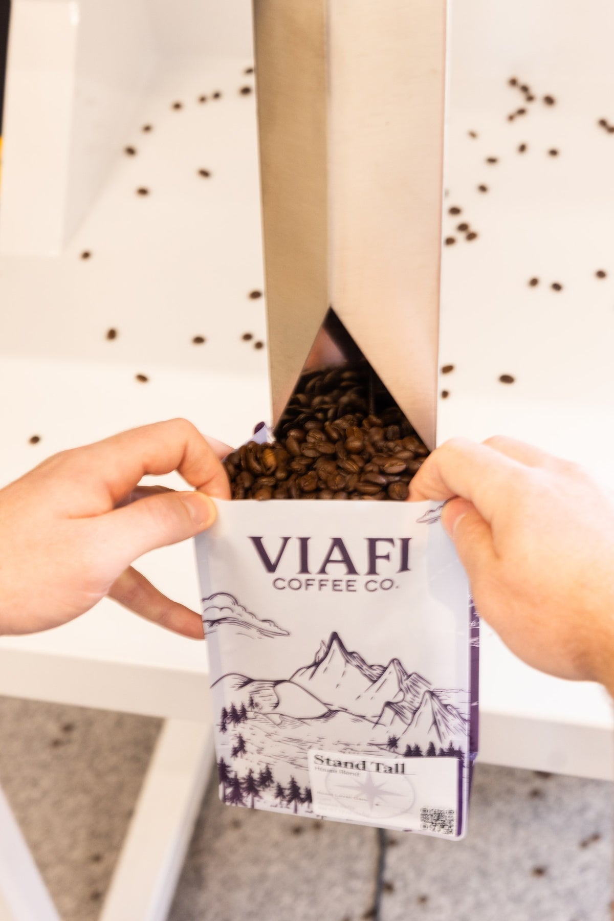 Roasted coffee beans pouring into a Viafi Stand Tall bag